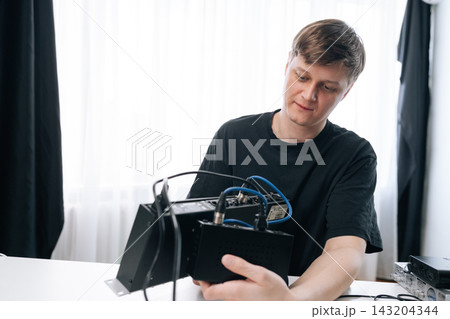 Young male audio engineer concentrating as he connecting cables and configures professional recording and mixing equipment at modern studio workstation, focused on sound production. Young male audio engineer concentrating as he connecting cables and configures professional recording and mixing equipment at modern studio workstation, focused on sound production. 143204344