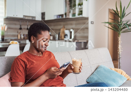 Young woman relaxing on the sofa, using smartphone and drinking coffee Young woman relaxing on the sofa, using smartphone and drinking coffee 143204480