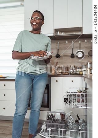 Young woman emptying the dishwasher in a modern kitchen Young woman emptying the dishwasher in a modern kitchen 143204484