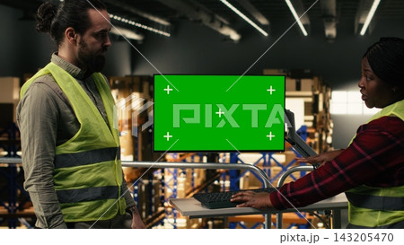 Green screen on monitor near multiethnic colleagues on industrial platform, man and woman working in fulfillment center focused on package handling and shipping management. Productivity. Green screen on monitor near multiethnic colleagues on industrial platform, man and woman working in fulfillment center focused on package handling and shipping management. Productivity. 143205470
