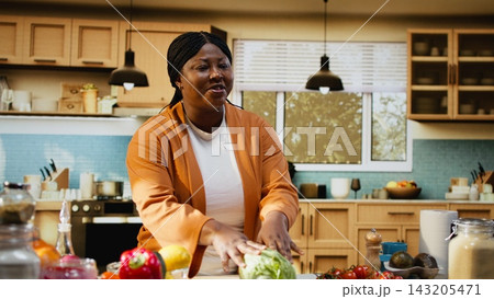 African American woman food vlogger filming homemade food recipe in a bright home kitchen. Solo influencer doing meal preparation with fresh ingredients for a salad, social media platforms. 143205471