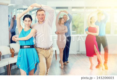 Positive man dancing playful Latin dance bachata with female partner during group class in studio Positive man dancing playful Latin dance bachata with female partner during group class in studio 143206603