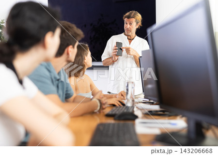 During computer courses, male teacher with mobile phone explains to listeners principle of operation 143206668