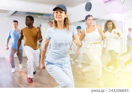Class of active young adult dancers performing steps during exercising modern dance together in dance hall Class of active young adult dancers performing steps during exercising modern dance together in dance hall 143206683