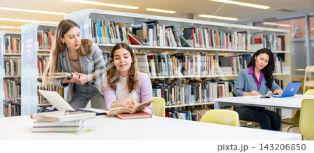 Two female students studying in library with books and laptop 143206850