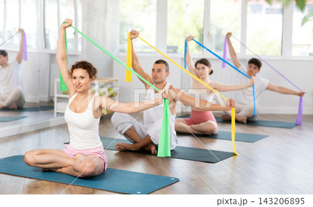Aerobics pilates women and men with rubber bands sitting on mats in sports studio 143206895