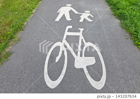 White pedestrian and bicycle symbols painted on asphalt path between grass lawns. Concept of urban infrastructure, shared path safety, cycling lane, walkable city White pedestrian and bicycle symbols painted on asphalt path between grass lawns. Concept of urban infrastructure, shared path safety, cycling lane, walkable city 143207634