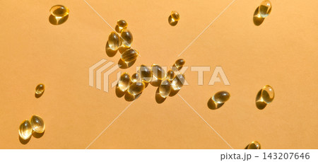 Golden capsules with nutritional vitamin or medicinal content on orange background, warm light, copy space. Concept of dietary supplements, healthy nutrition, wellness, diet Golden capsules with nutritional vitamin or medicinal content on orange background, warm light, copy space. Concept of dietary supplements, healthy nutrition, wellness, diet 143207646