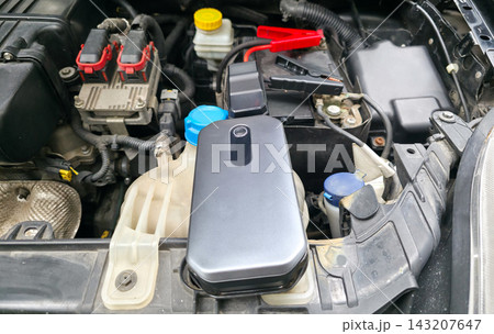 Portable jump starter connected to car battery under open hood, no people. Concept of roadside assistance, emergency car repair, travel safety, road trip preparedness 143207647