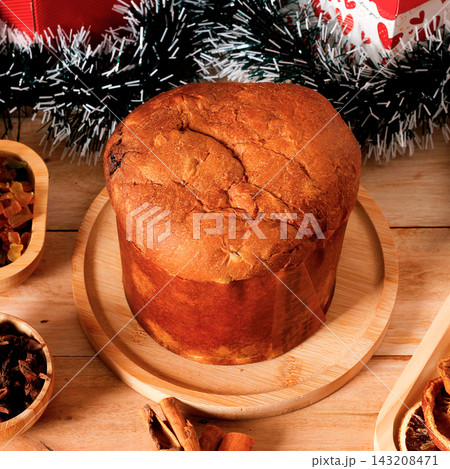 Traditional Christmas panettone filled with candied fruit and raisins, set in a festive atmosphere on a rustic wooden table. 143208471