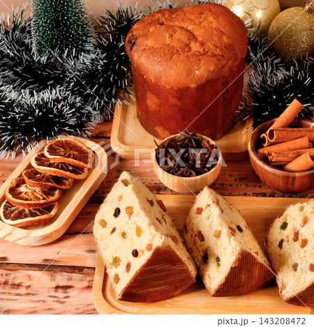 Christmas panettone with candied fruit and raisins featured on a festive table, with slices cut to reveal the soft crumb. 143208472