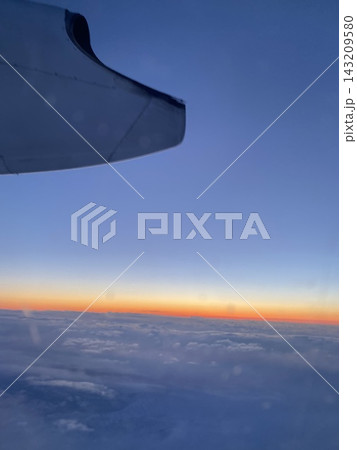 飛行機の機窓から望む夕暮れの雲海と青からオレンジに染まる空 143209580