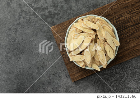 Slices of dried astragalus root in a ceramic bowl placed on a wooden board, traditional Chinese medicine 143211366