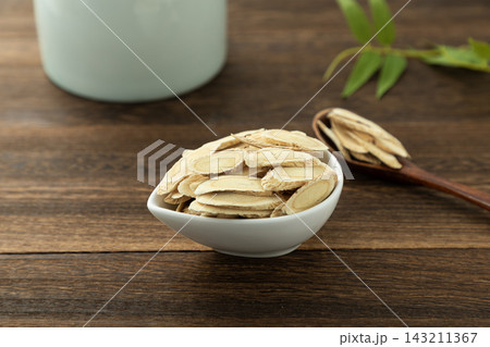 Slices of Chinese herbal medicine Huang Qi or Astragalus in a white bowl on wooden background Slices of Chinese herbal medicine Huang Qi or Astragalus in a white bowl on wooden background 143211367