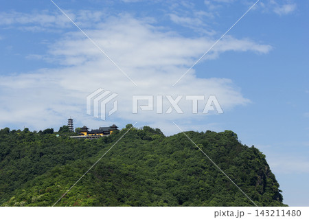 Buddhist temple and pagoda situated on a lush green forested mountain peak under a clear blue sky with white clouds 143211480