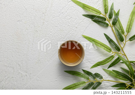 Top view of a small cup of tea on a white textured background with green bamboo leaves and copy space Top view of a small cup of tea on a white textured background with green bamboo leaves and copy space 143211555