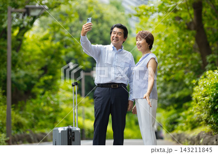 緑の中でスマートフォンで写真を撮るシニア夫婦 143211845