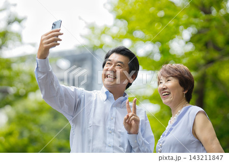 緑の中でスマートフォンで写真を撮るシニア夫婦 緑の中でスマートフォンで写真を撮るシニア夫婦 143211847