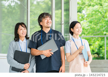 施設の玄関前で笑顔を見せる医師と女性介護スタッフ。医療と介護を支える3人のチームワーク 143214723