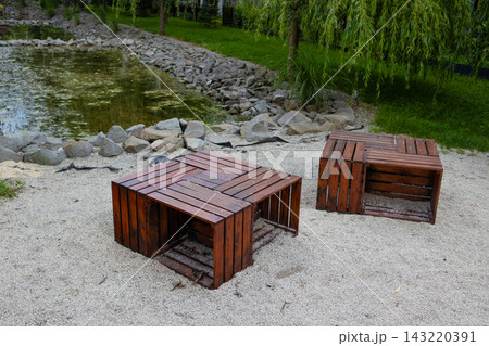 Modern wooden pallet benches on pebble beach near small pond in public park, outdoor lounge area 143220391