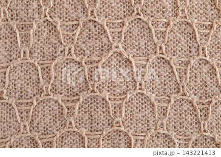 Close-up of beige knitted fabric showing the texture of the yarn and the hand-knit pattern. Close-up of beige knitted fabric showing the texture of the yarn and the hand-knit pattern. 143221413