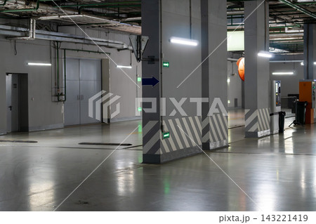 Empty Underground Parking Garage Interior With Concrete Pillars, Directional Signs and Reflective Floor Lighting Empty Underground Parking Garage Interior With Concrete Pillars, Directional Signs and Reflective Floor Lighting 143221419