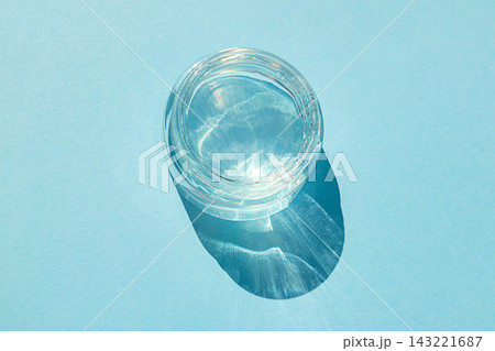Top view of a glass jar of water casting a shimmering shadow on blue paper 143221687