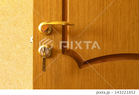 Close-up of wooden interior door with gold-colored curved handle and key inserted into lock. Warm wood grain and polished metal hardware emphasize home security, privacy, access, protection, locking 143221852