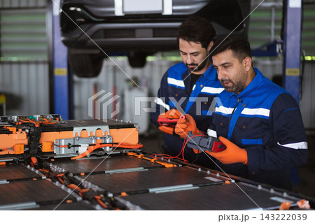 Technicians using multimeter to test EV battery pack in garage 143222039