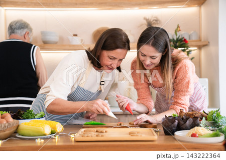 Caucasian daughter and mother decorating gingerbread cookies with icing at home 143222364