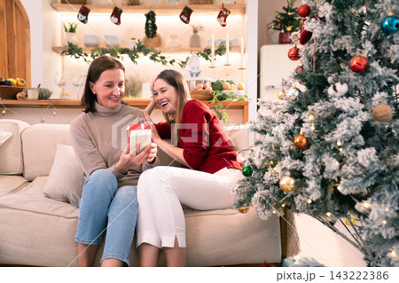 Happy daughter surprising mother with wrapped gift box during Christmas Happy daughter surprising mother with wrapped gift box during Christmas 143222386