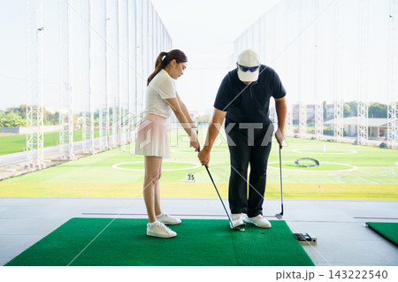 Asian female golfer practicing swing with male coach at driving range Asian female golfer practicing swing with male coach at driving range 143222540