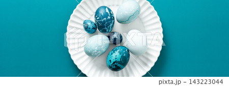 Colorful blue Easter eggs are artistically arranged on a white plate resting on a vibrant teal surface, capturing the essence of spring festivities and holiday traditions, banner Colorful blue Easter eggs are artistically arranged on a white plate resting on a vibrant teal surface, capturing the essence of spring festivities and holiday traditions, banner 143223044
