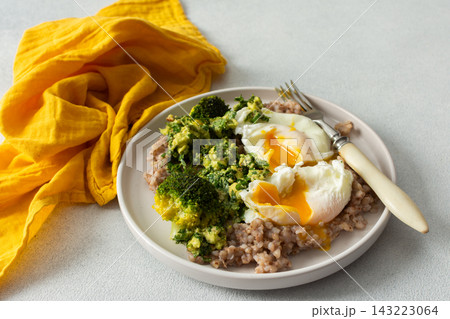 A healthy breakfast bowl features green buckwheat topped with pesto, steamed broccoli, and poached eggs. A fork rests beside the dish ready for a nutritious meal 143223064