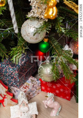 A Christmas tree stands in a warm room filled with decorations. Colorful ornaments hang from the branches while lights add a festive touch. People gather around to enjoy the holiday spirit 143223066