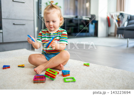 Little girl playing colorful magnet plastic blocks kit at home. The child playing educational games. Early childhood development. 143223694