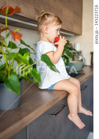 Baby girl blonde eating an apple in the kitchen, concept of healthy food for children 143223716
