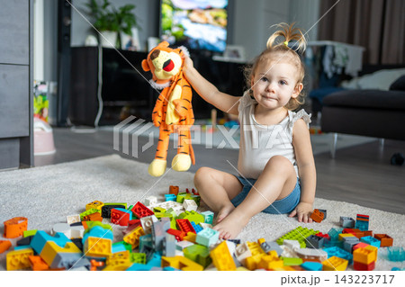 Caucasian child a little girl is playing in the constructor at home. Educational toys for children. Caucasian child a little girl is playing in the constructor at home. Educational toys for children. 143223717