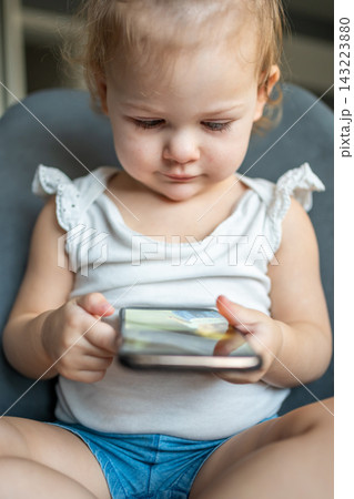 Smiling little girl is sitting on armchair and using smart phone Smiling little girl is sitting on armchair and using smart phone 143223880