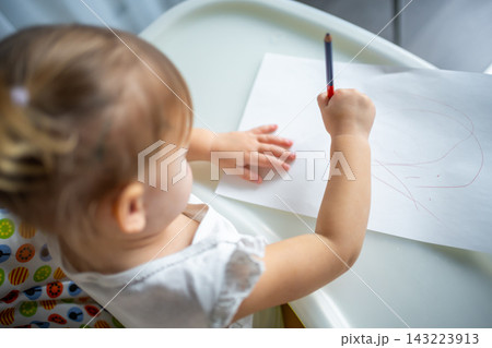 Cute little girl painting with red pencil at home. Creative games for kids. Stay at home entertainment 143223913