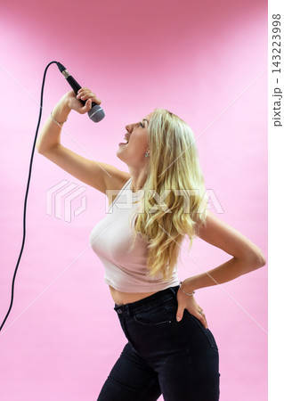 Beautiful young woman with microphone singing on pink background Beautiful young woman with microphone singing on pink background 143223998