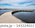 Calm lake and wooden pier under a blue sky with fluffy clouds. 143224022