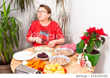 A woman is chopping onions in the kitchen while preparing Herring Under Fur Coat salad, the traditional Ukrainian Christmas salad Shuba. Nearby are plates with carrots, potatoes, beets, and fish A woman is chopping onions in the kitchen while preparing Herring Under Fur Coat salad, the traditional Ukrainian Christmas salad Shuba. Nearby are plates with carrots, potatoes, beets, and fish 143226359