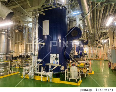Industrial interior of vessel engine room displaying a large vertical marine auxiliary boiler with insulated steam pipelines. Industrial interior of vessel engine room displaying a large vertical marine auxiliary boiler with insulated steam pipelines. 143226474