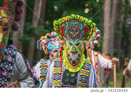 Kukeri Ritual Mask. Kukeri performer wearing ornate colorful ritual mask and traditional Bulgarian costume with decorative beadwork, cowbells. Bulgarian folklore, masquerade tradition, heritage Kukeri Ritual Mask. Kukeri performer wearing ornate colorful ritual mask and traditional Bulgarian costume with decorative beadwork, cowbells. Bulgarian folklore, masquerade tradition, heritage 143226593