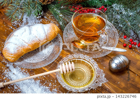 Christmas background, cup of tea with honey and croissant, branch of a Christmas tree in the snow Christmas background, cup of tea with honey and croissant, branch of a Christmas tree in the snow 143226746