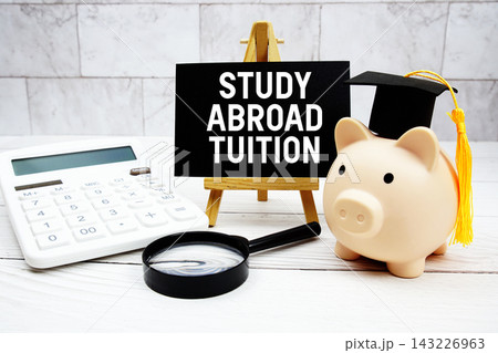 Study Abroad Tuition text with mortarboard, piggy bank, calculator, magnifying glass 143226963