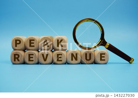 Peak Revenue alphabet letters wooden cube and magnifying glass on blue background Peak Revenue alphabet letters wooden cube and magnifying glass on blue background 143227030