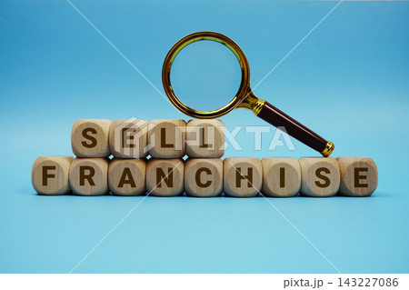 Sell Franchise alphabet letters wooden cube and magnifying glass on blue background Sell Franchise alphabet letters wooden cube and magnifying glass on blue background 143227086