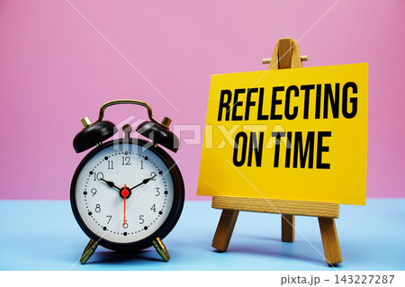 Reflecting On Time text with alarm clock on pink and blue background Reflecting On Time text with alarm clock on pink and blue background 143227287